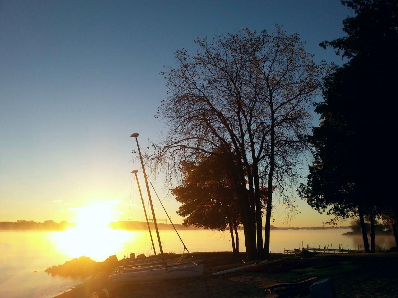 A lakeside view with boats and trees during sunset.