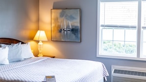 A neatly made bed with a quilted blanket, a bedside lamp, and a framed painting of sailboats on the wall. - Beach Harbor Resort (Sturgeon Bay)