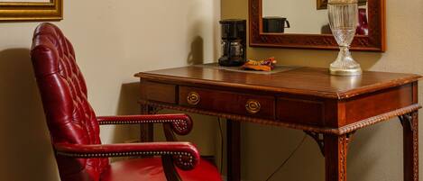 A room with a red leather chair, a wooden desk, a lamp, a framed picture, and a large mirror.