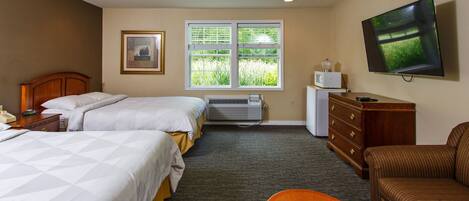A hotel room with two beds, a TV, a dresser, and a window with a view of greenery.