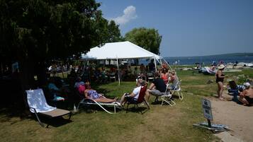 A beachside gathering with people relaxing under a white tent.