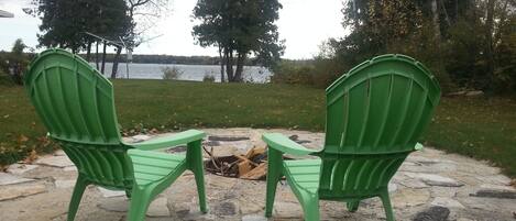 Dos sillas Adirondack verdes mirando un brasero de piedra con vista al lago.