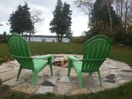Dos sillas Adirondack verdes mirando un brasero de piedra con vista al lago.