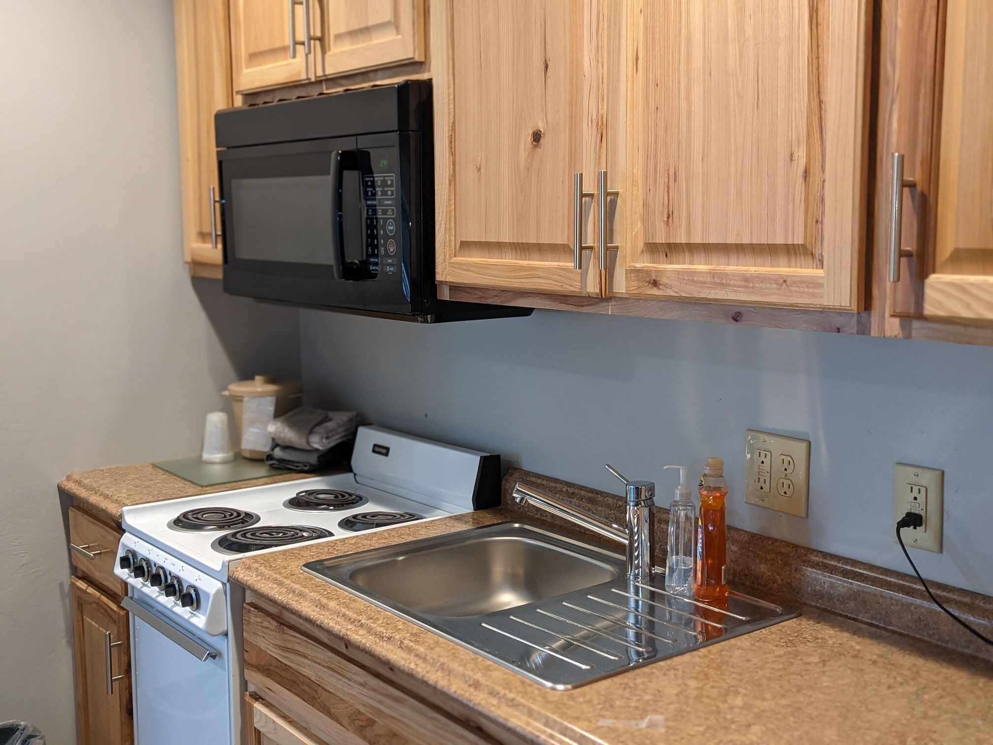 A kitchen with wooden cabinets, a black microwave, a white stove, and a stainless steel sink.
