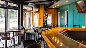 A restaurant interior with wooden tables and chairs, a bar area, and large windows allowing natural light. - Beach Harbor Resort (Sturgeon Bay)