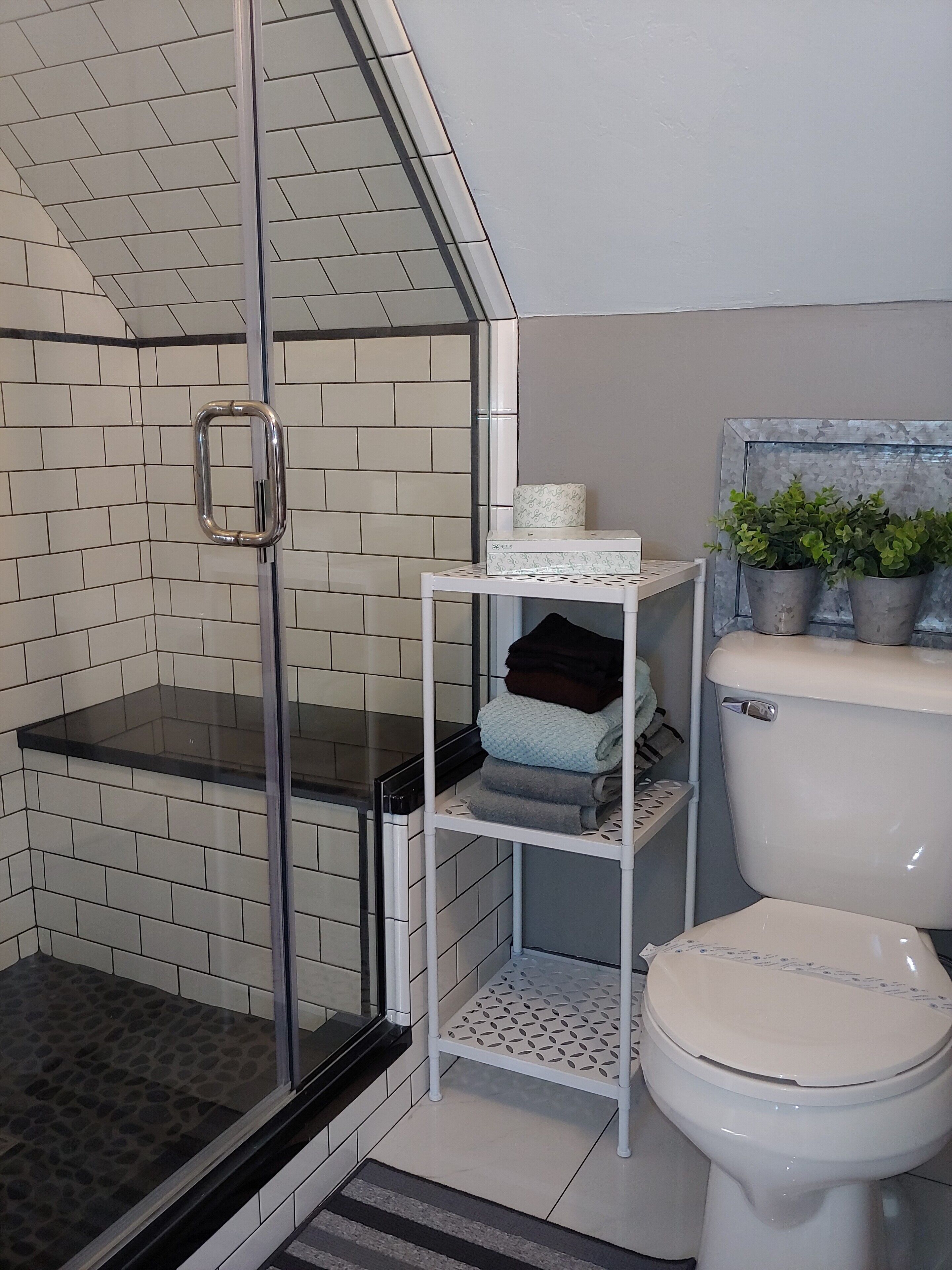 A bathroom with a glass shower enclosure, a toilet, and a shelf with towels and a toilet paper holder.
