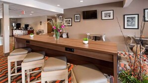 Un área de recepción con mostrador de madera, taburetes tipo bar, cuadros en la pared y un televisor.