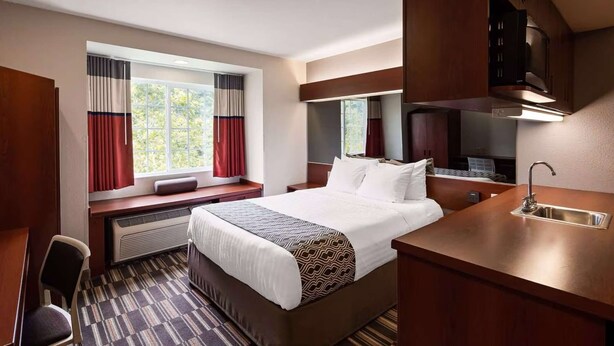Una habitación de hotel con cama, escritorio, silla, ventana con cortinas, microondas integrado y lavamanos.