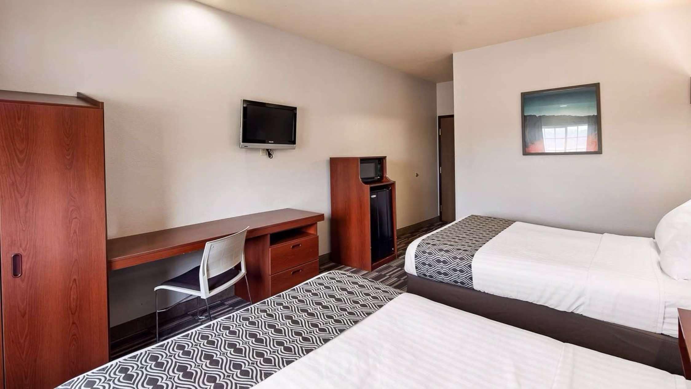 A hotel room with two beds, a desk, a chair, a television, and a small cabinet.