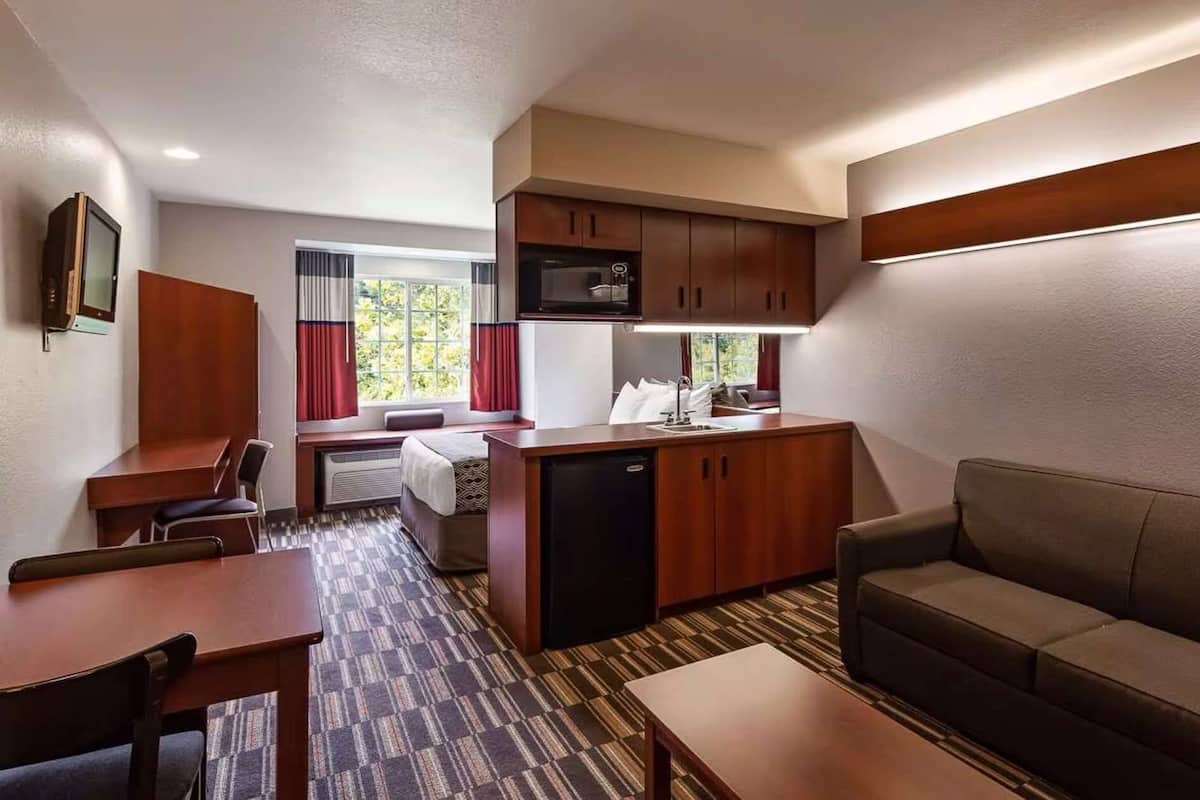 A compact hotel room with a kitchenette, a sofa, a dining table, and a TV.