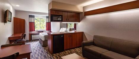 A compact hotel room with a kitchenette, a sofa, a dining table, and a TV.
