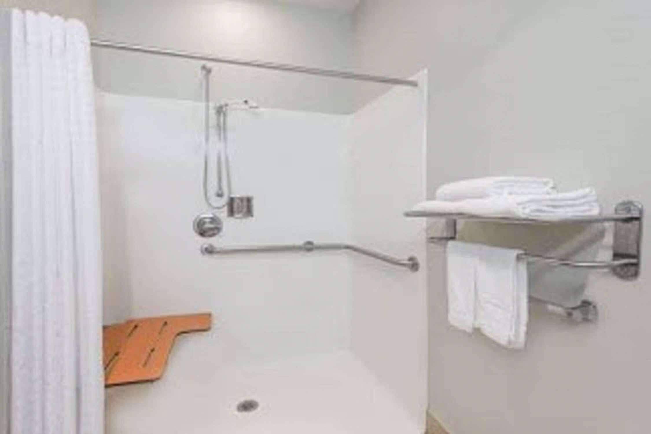 A modern bathroom with a walk-in shower, a towel rack, and a wooden bench.