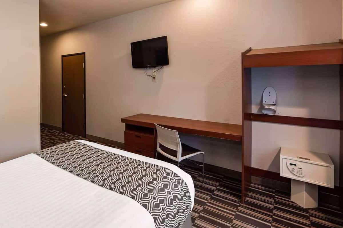 A hotel room with a bed, a desk, a chair, a TV, and a minibar.