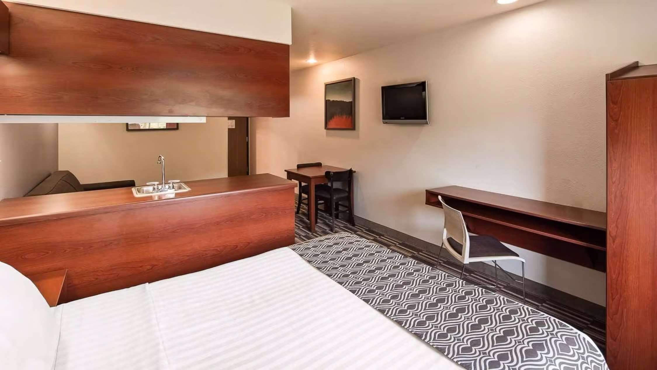 A hotel room with a bed, a wooden desk, a small table, a TV, and a mirror.