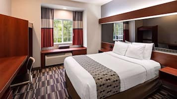 A hotel room with a large bed, a desk, a chair, a window with curtains, and a mirror.