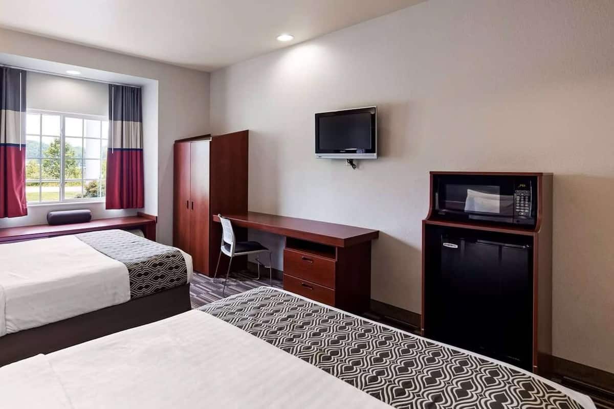 A hotel room with two beds, a desk, a chair, a TV, and a minibar.