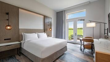 Habitación de hotel moderna con una cama grande, un escritorio y una silla. Se ve follaje verde a través de la ventana.
