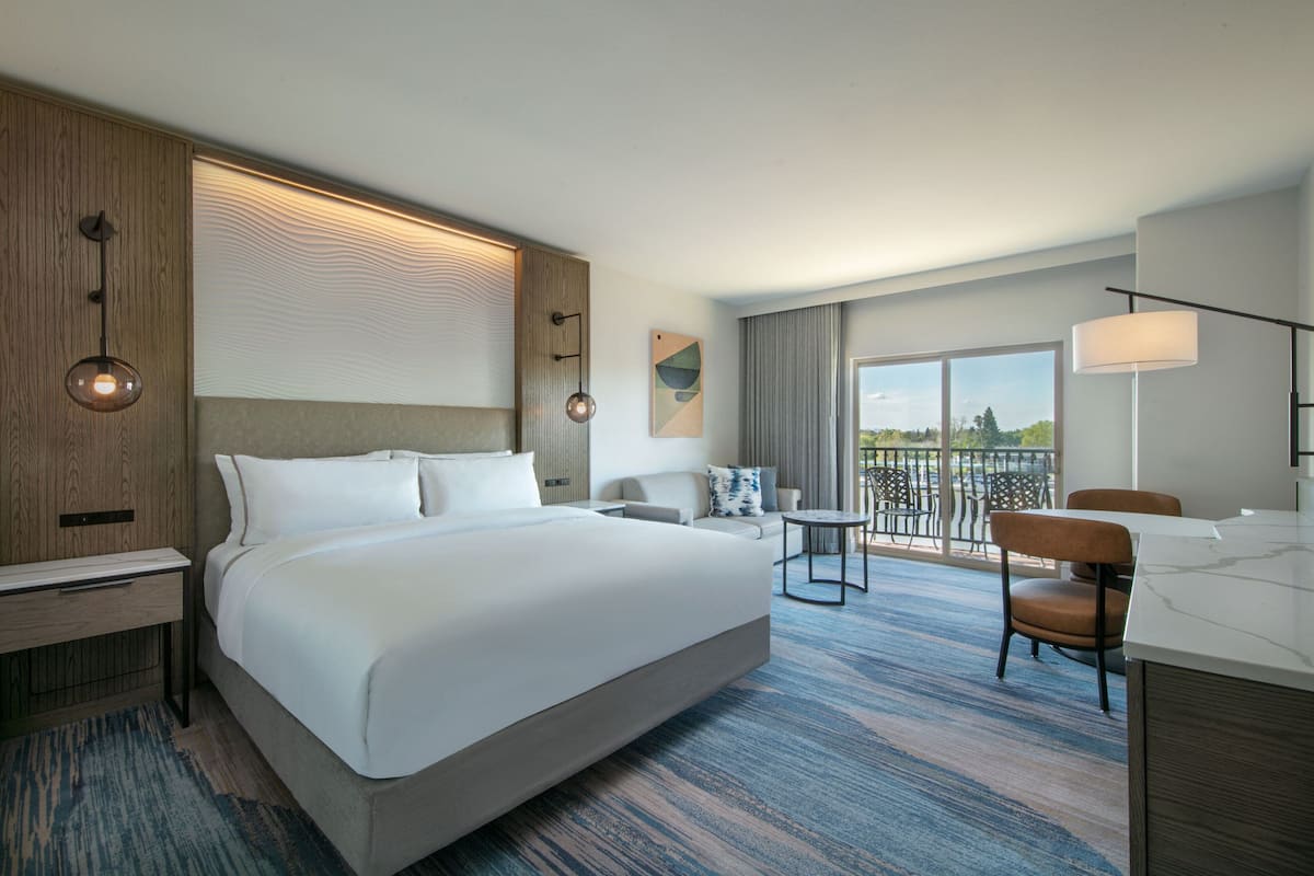 Habitación de hotel moderna con una cama grande, un escritorio, una silla, una mesita y un balcón con vistas.