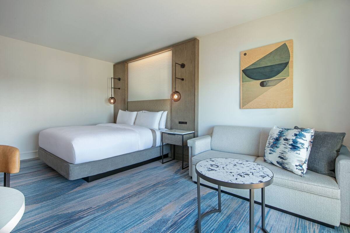 Una habitación de hotel con una cama, un sofá, una mesita y una obra de arte en la pared.