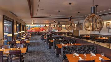 A restaurant with multiple dining areas, including booths and tables, with overhead lighting and a colorful mural on the back wall.
