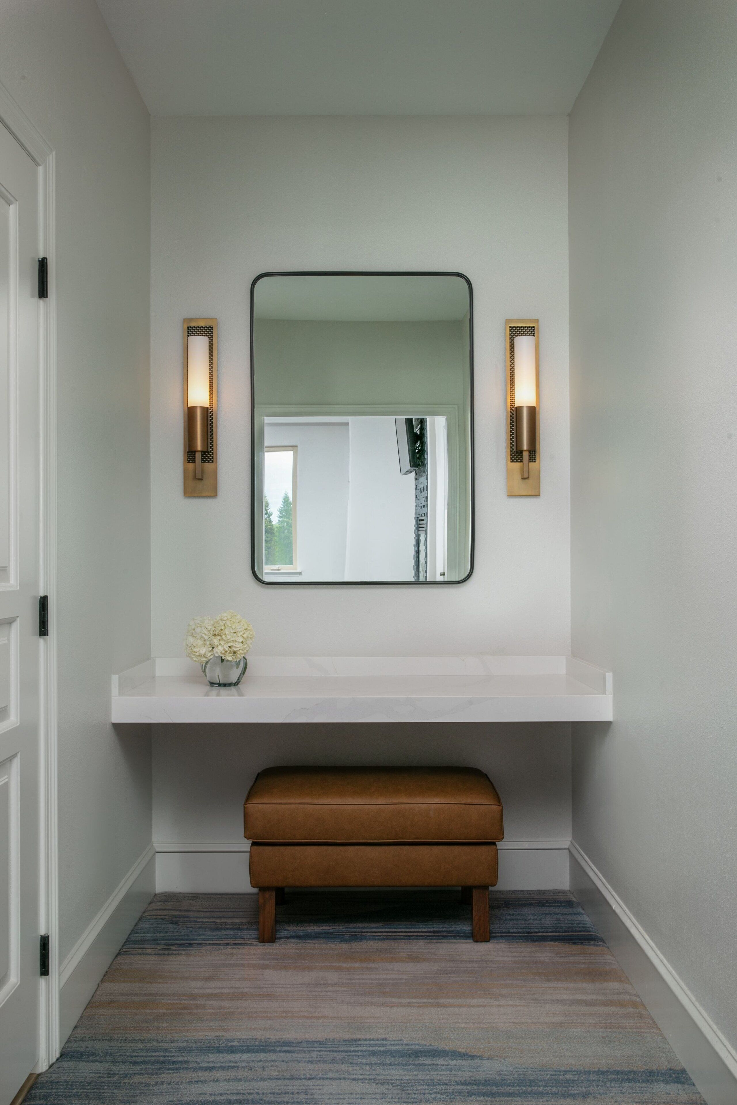 A hallway with a white bench, a mirror, and two wall sconces.