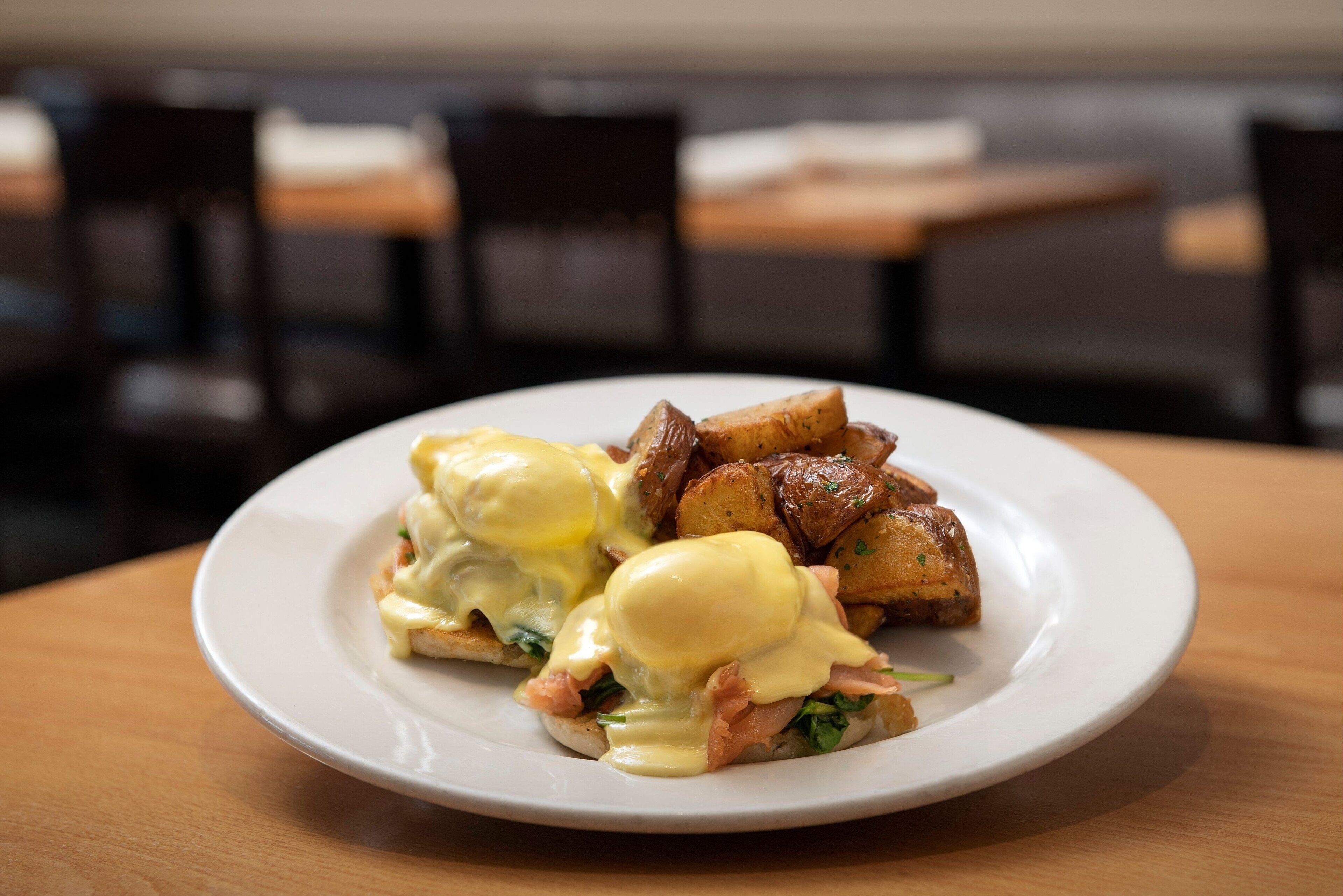 Um prato de ovos Benedict com presunto e batatas sobre um prato branco.