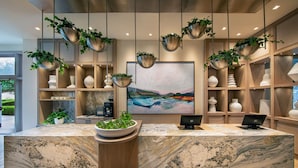 Een receptiegedeelte met een marmeren balie, hangplanten, een groot schilderij en planken met decoratieve objecten.