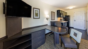 Une chambre d’hôtel moderne équipée d’une télévision à écran plat, d’un bureau avec des tiroirs, d’un coin repas avec des chaises, d’un four à micro-ondes et d’un réfrigérateur.