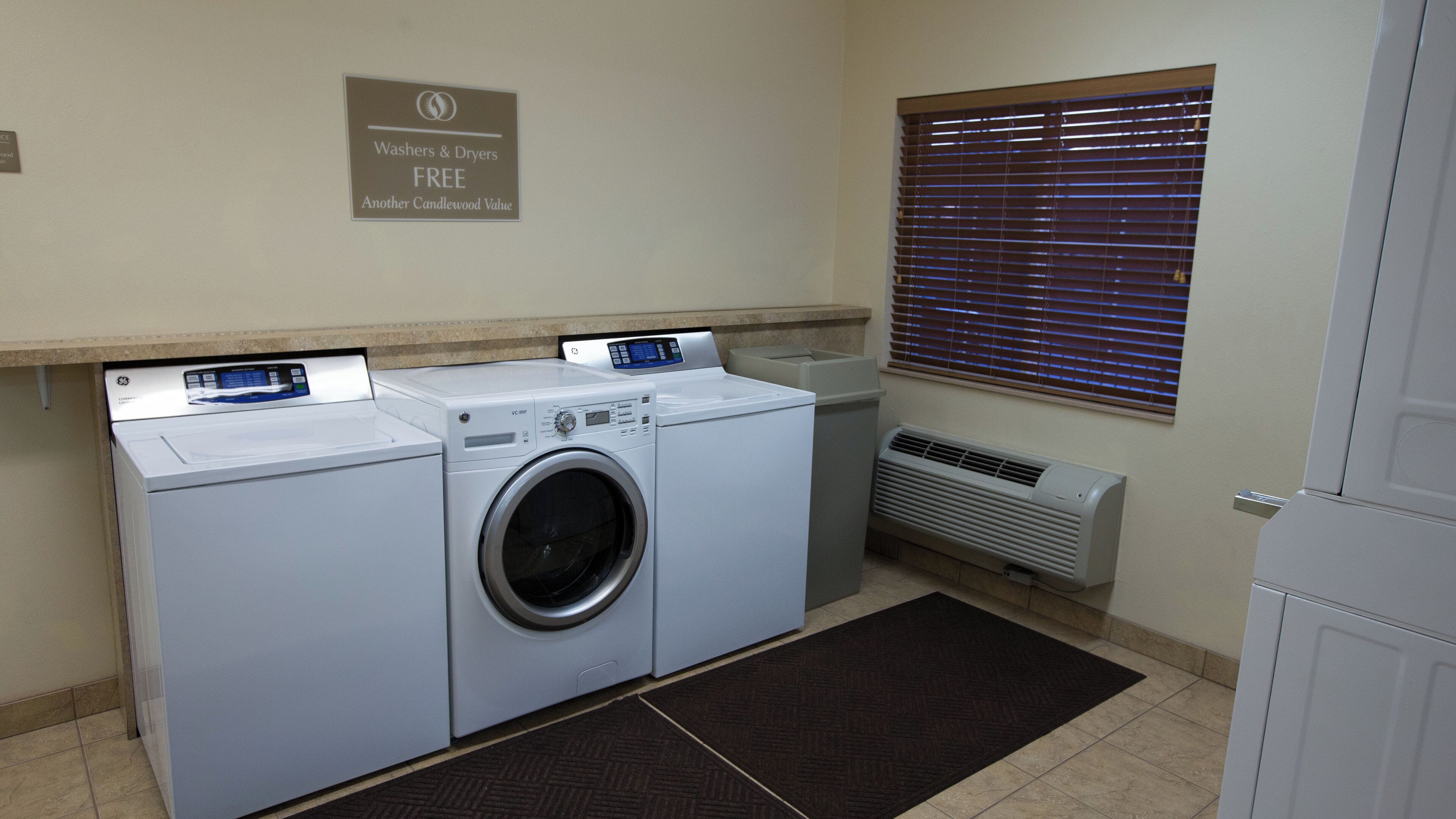 A laundry room with two front-loading washers and dryers, a sign indicating free washers and dryers, a vent, and a window with blinds.
