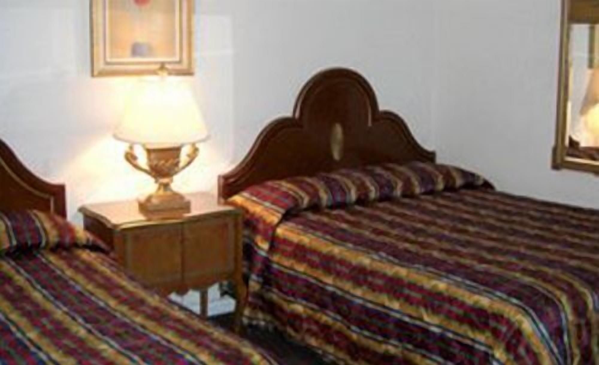 Een hotelkamer met twee bedden, een nachtkastje met een lamp en een lijst met een foto aan de muur.