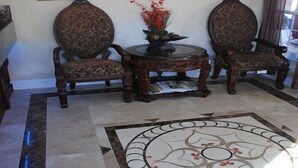 A room with a patterned carpet, two ornate chairs, a small table with a vase of flowers, and framed pictures on the walls. - Travel Inn And Suites (Victorville)