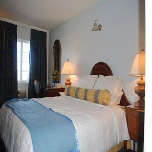 Uma cama bem arrumada com um cobre-leito azul e branco, duas luminárias de cabeceira e uma cabeceira de madeira.