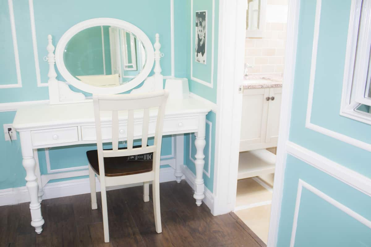 A white vanity with a round mirror, a white chair, and a blue wall.