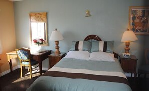 Um quarto bem arrumado com uma cama grande, duas mesas de cabeceira com abajures, uma cadeira e uma escrivaninha com luminária.