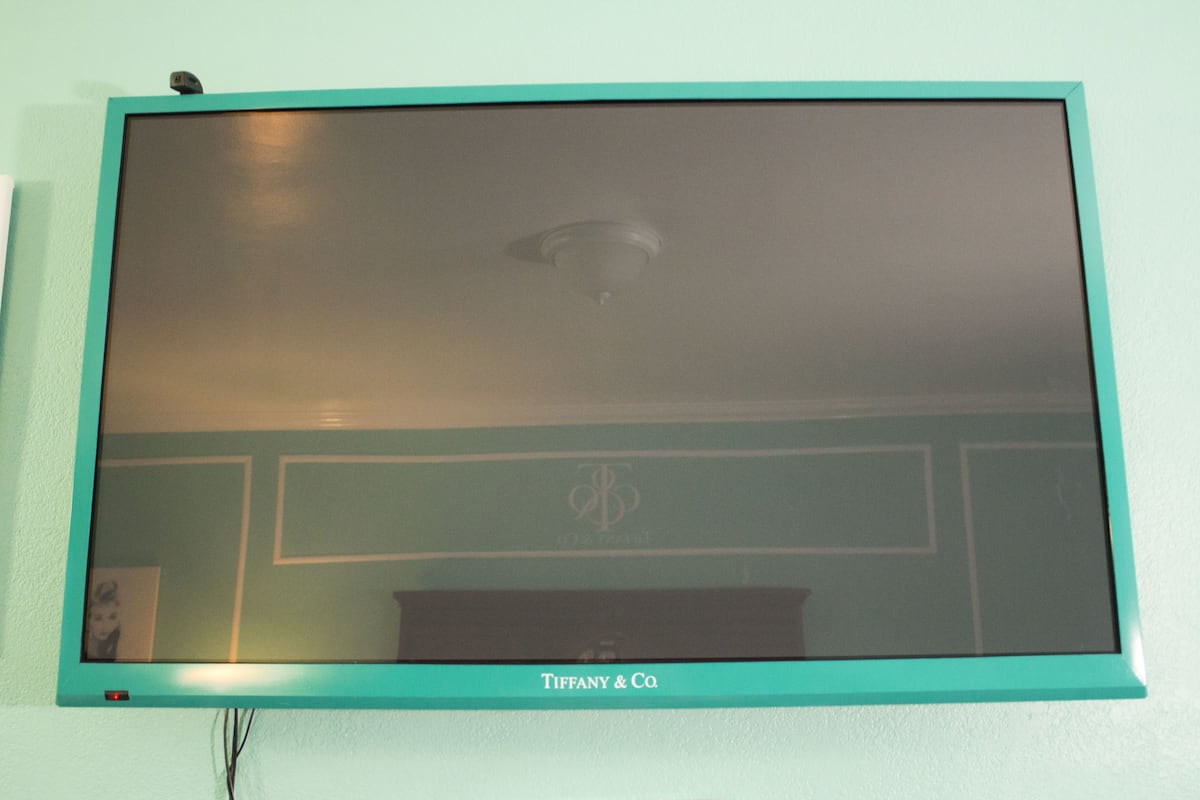 A flat-screen TV mounted on a teal wall with a visible logo and a power cord.