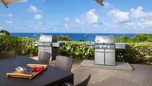 Een terras met een eethoek, twee barbecuegrills, bestek en uitzicht op de oceaan.