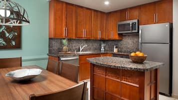 Una cocina con gabinetes de madera, encimera de granito, microondas, refrigerador y un comedor con mesa y sillas.