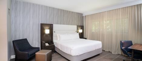 A hotel room with a large bed, two bedside tables, a desk, a chair, and a small ottoman.