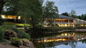 A modern building with large glass windows, a reflection in a pond, and a well-maintained garden. - Crowne Plaza Atlanta SW - Peachtree City by IHG (Peachtree City)