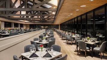 Un comedor amplio con mesas largas, vigas de madera modernas y ventanas grandes que dejan entrar luz natural.