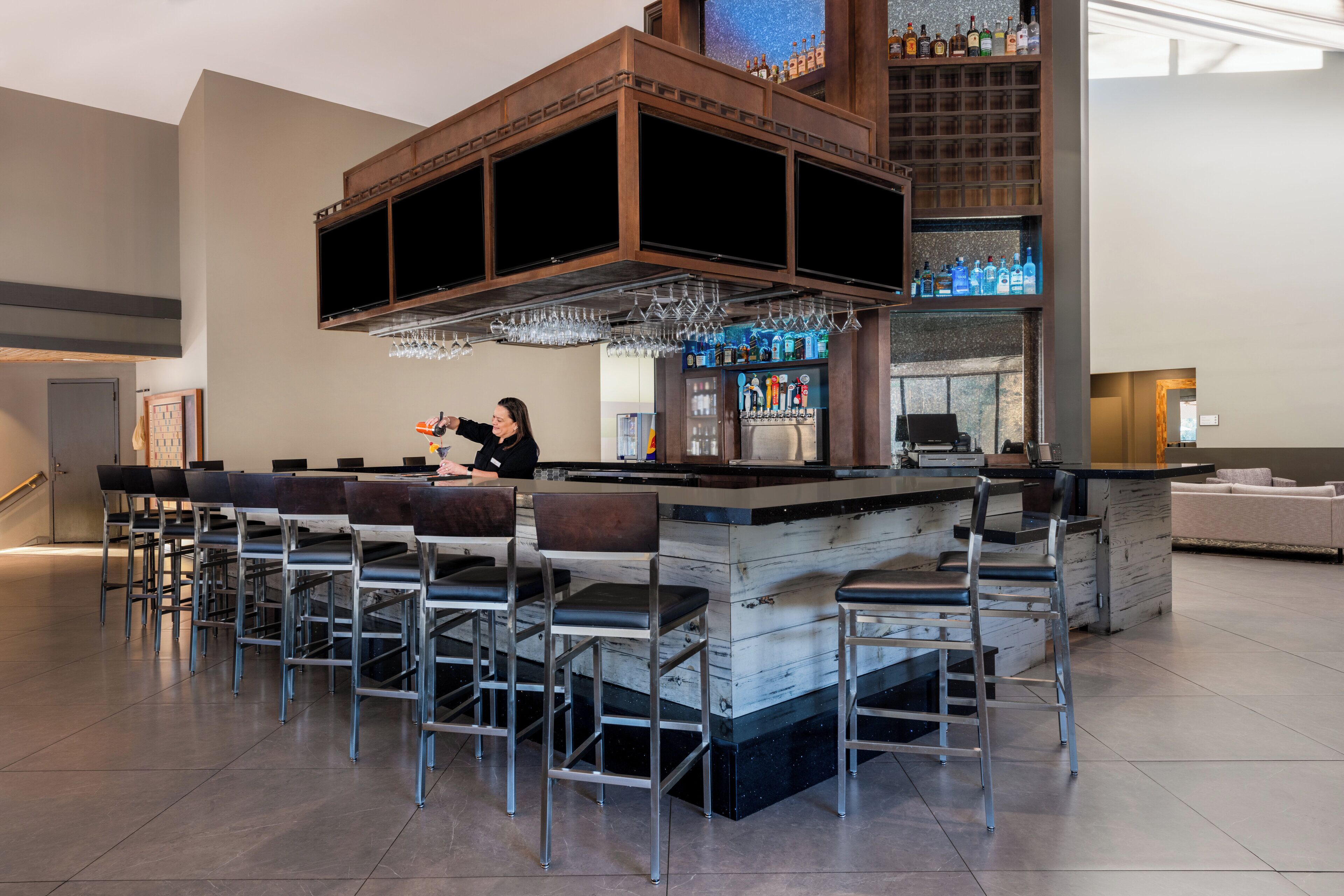 A bar area with a bartender, bar stools, a wine cooler, and a large selection of bottles.