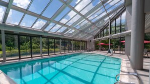 An indoor swimming pool with a glass ceiling, clear blue water, and a view of greenery outside. - Crowne Plaza Atlanta SW - Peachtree City by IHG (Peachtree City)