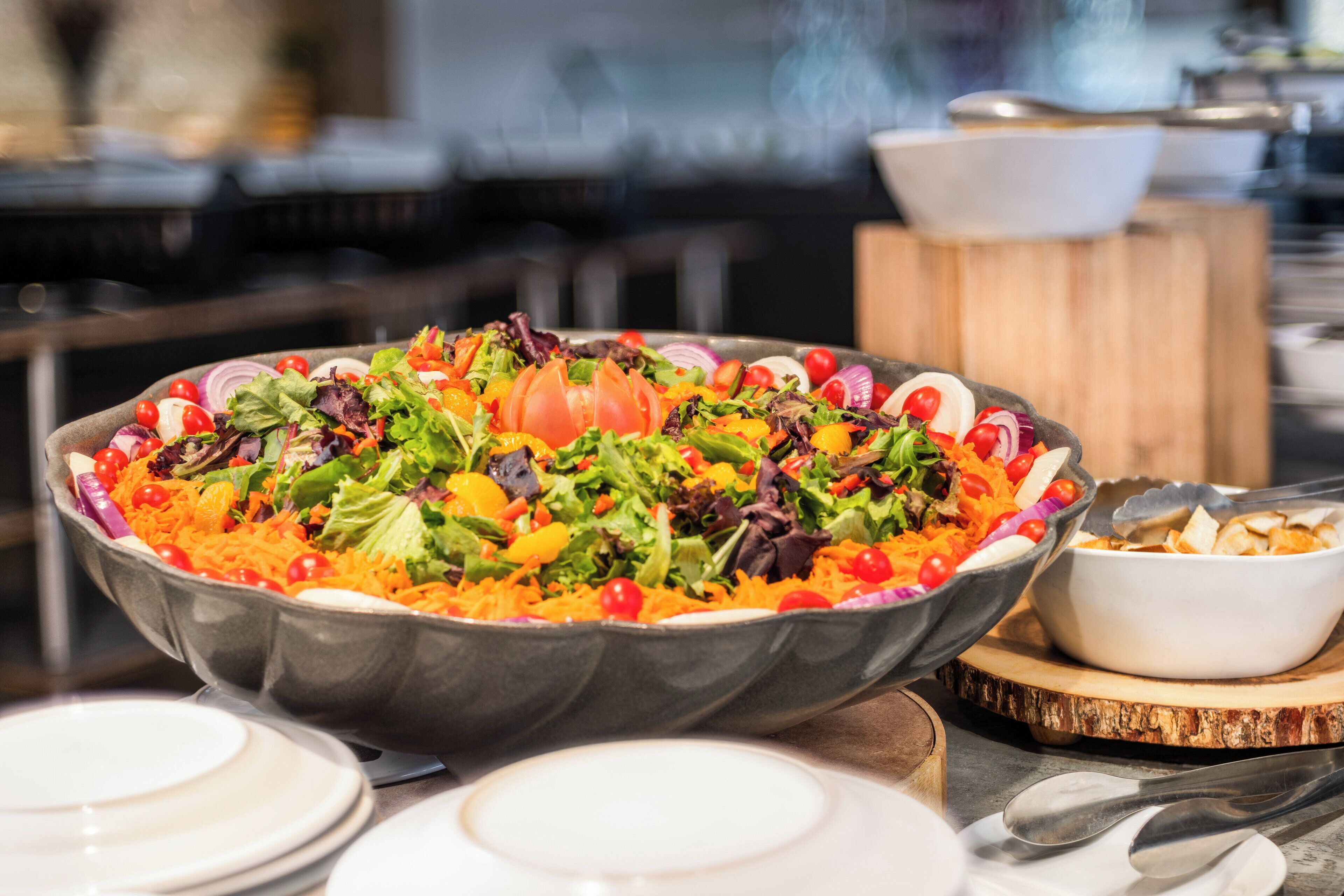 A large salad bowl with various vegetables and a white bowl with chips on a wooden board.