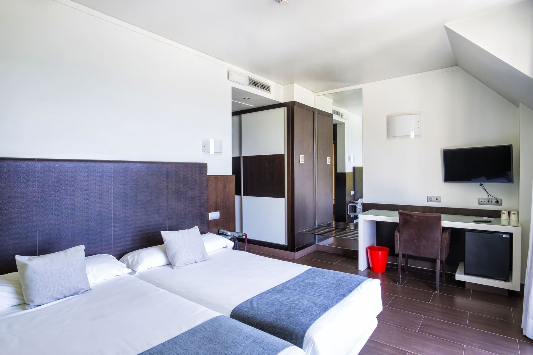 Habitación de hotel con dos camas, un escritorio, televisión y zona de ducha.