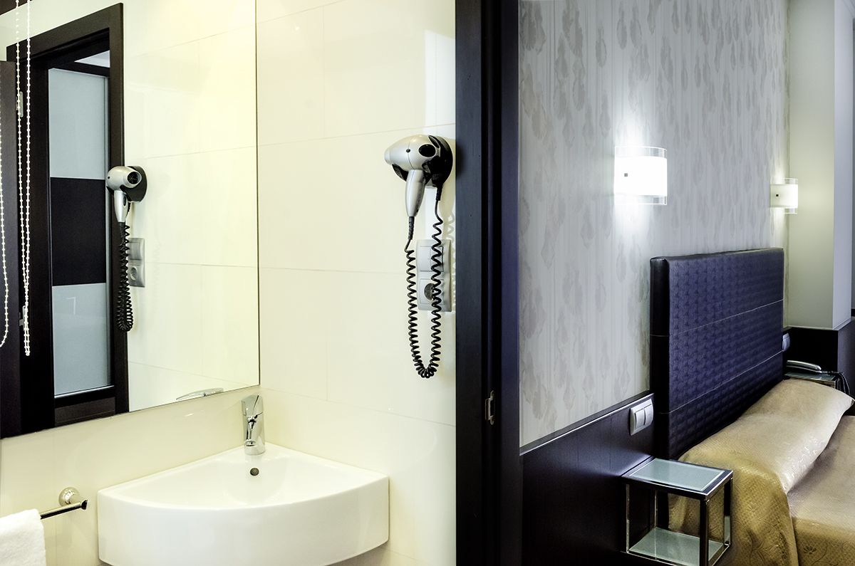 A hotel room with a white sink, a hairdryer, and a bed with a headboard.