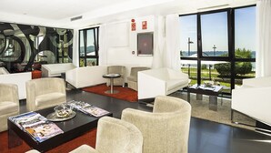 A modern hotel room with a large window offering a view of the sea, a seating area with white sofas and armchairs, and a coffee table with magazines. - Hotel Carril (Vilagarcia de Arousa)