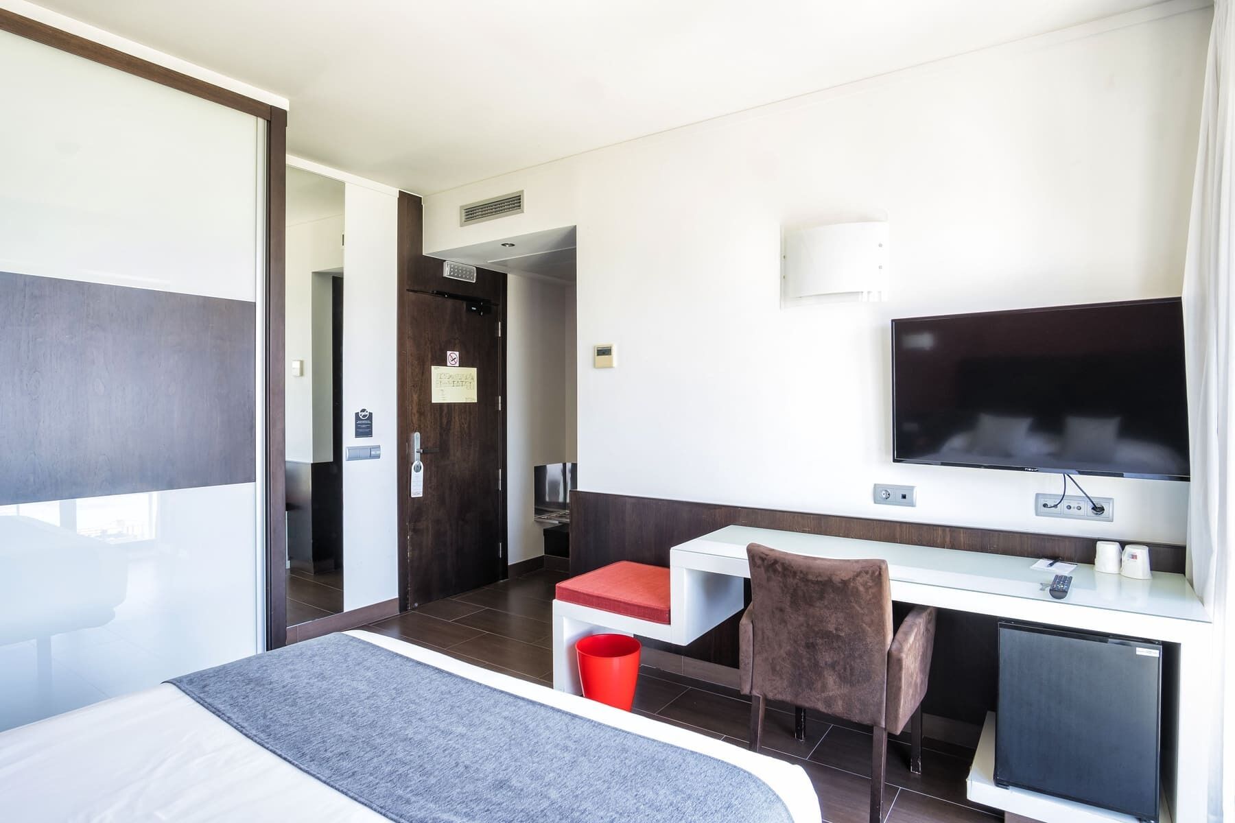 Habitación de hotel con cama, escritorio, silla, televisión y un refrigerador pequeño.