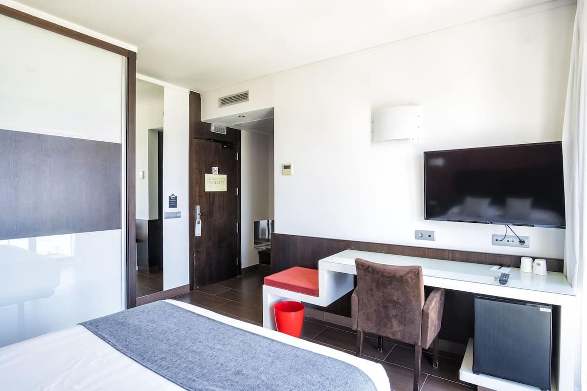 Habitación de hotel con cama, escritorio, silla, televisión y un refrigerador pequeño.