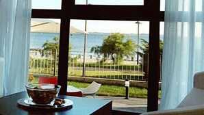 A room with a large window offering a view of the sea and a beach. There is a table with a bowl and a cup on it. - Hotel Carril (Vilagarcia de Arousa)