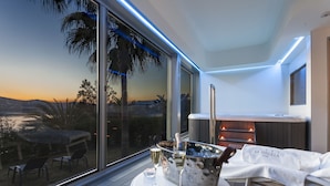 En moderne balkon med udsigt til solnedgangen, et spabad samt et bord med champagnekøler og glas.